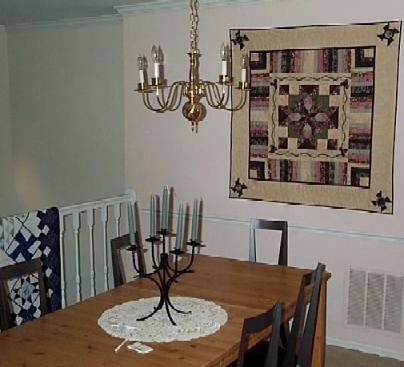 Picture of dining room with burgandy progressive quilt on wall and bit of blue and white quilt.