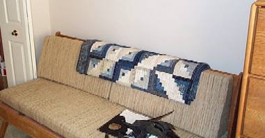 Picture of couch with log cabin style blue and white quilt.
