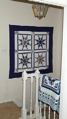 Picture of Feathered Star quilt on wall and blue quilt over rail.