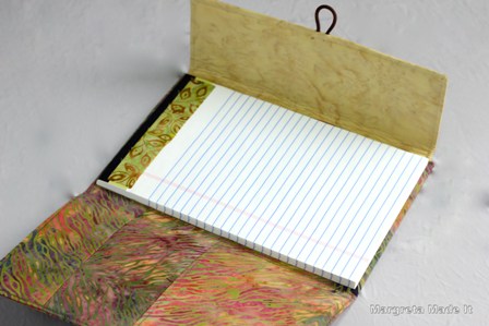 Refillable cover for junior legal pads. Includes a pocket for other papers along with the writing pad. Has an elastic loop and button closure. Green, orange, brown, rust batik fabrics.