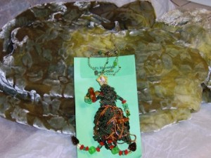 Oaken Oma wearable art pin in browns and greens teamed with a multi-shaded green scarf